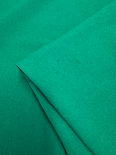 A close-up of Super Cheap Fabrics' Cotton Lycra - Deep Mint - 165cm, neatly folded to showcase its bright green color, visible soft texture, and smooth surface.
