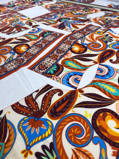 A close-up of Super Cheap Fabrics' 100% Cotton Voile - 130cm panel shows vibrant paisley and floral patterns in orange, blue, brown, and yellow with geometric borders. The fabric measures 130cm (length) x 140cm (width) laid flat.
