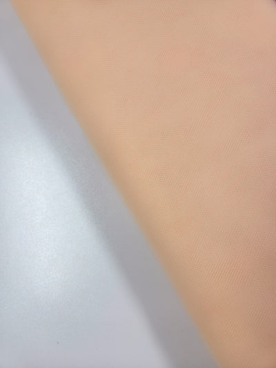 A close-up of Super Cheap Fabrics’ Soft Tulle - Peach - 150cm on a white surface highlights its soft, slightly textured look—ideal for sheer, lightweight projects like bridal veils.