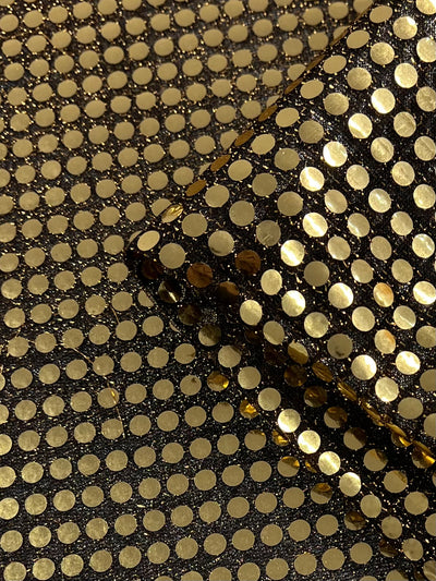 Close-up of Sequin - Black Gold fabric (112cm) by Super Cheap Fabrics, with shiny gold dot pattern on black—perfect for dancewear or costumes. One piece is folded over another, showcasing its reflective metallic finish.