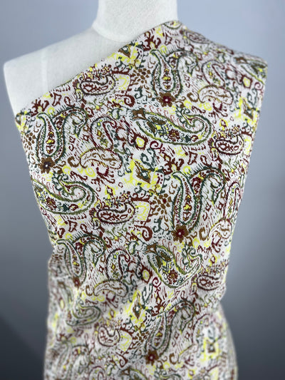 A mannequin is draped with the Voile - Paisley - 145cm by Super Cheap Fabrics, featuring green, yellow, and maroon intricate paisley on white. Ideal for warm weather clothing.