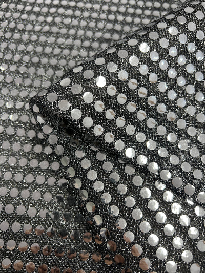 A close-up of Super Cheap Fabrics’ Sequin - Black & Silver (112cm) shows black mesh dancewear fabric adorned with shiny silver sequins in a regular grid, creating a reflective, textured look.