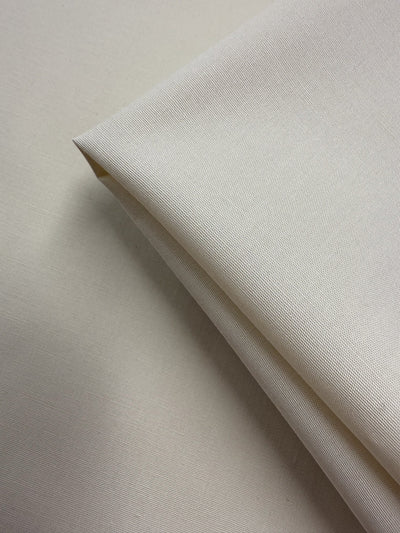 A close-up of Super Cheap Fabrics’ Stretch Cotton in Antique White (147cm), folded over a flat layer to display its fine weave, light weight, soft color, and 97% cotton composition.