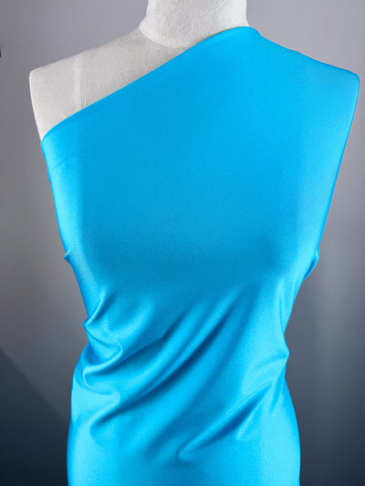 A white mannequin showcases Super Cheap Fabrics’ Nylon Lycra - Blue Atoll (154cm), a bright blue, four-way stretch fabric with a satin-like sheen. The swimwear-inspired material drapes smoothly, creating soft folds and a sleek silhouette.