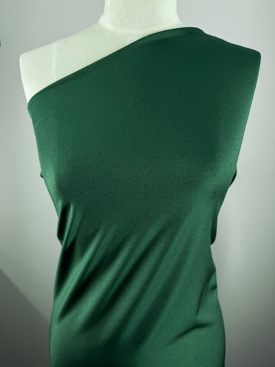 A mannequin displays a fitted, one-shoulder garment in Super Cheap Fabrics’ Nylon Lycra – Dark Green (154cm), featuring a smooth texture and four-way stretch, set against a plain light background.