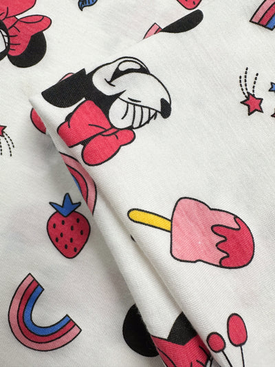 The "Printed Jersey - Minni Summer - 150cm" from Super Cheap Fabrics features a medium-weight, two-way stretch fabric adorned with whimsical prints of a cartoon character, strawberries, popsicles, stars, and rainbows in lively pink, red, black, blue, and white hues.
