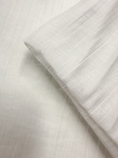 A close-up of Super Cheap Fabrics' Textured Designer Voile - Ivory - 155cm, showcasing its light color, soft texture, and slightly wrinkled look as it rests on matching fabric.