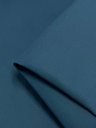 A close-up of the folded Gabardine fabric in teal from Super Cheap Fabrics showcases its smooth texture and rich color. This durable, wrinkle-resistant material subtly captures light on its tightly woven surface.