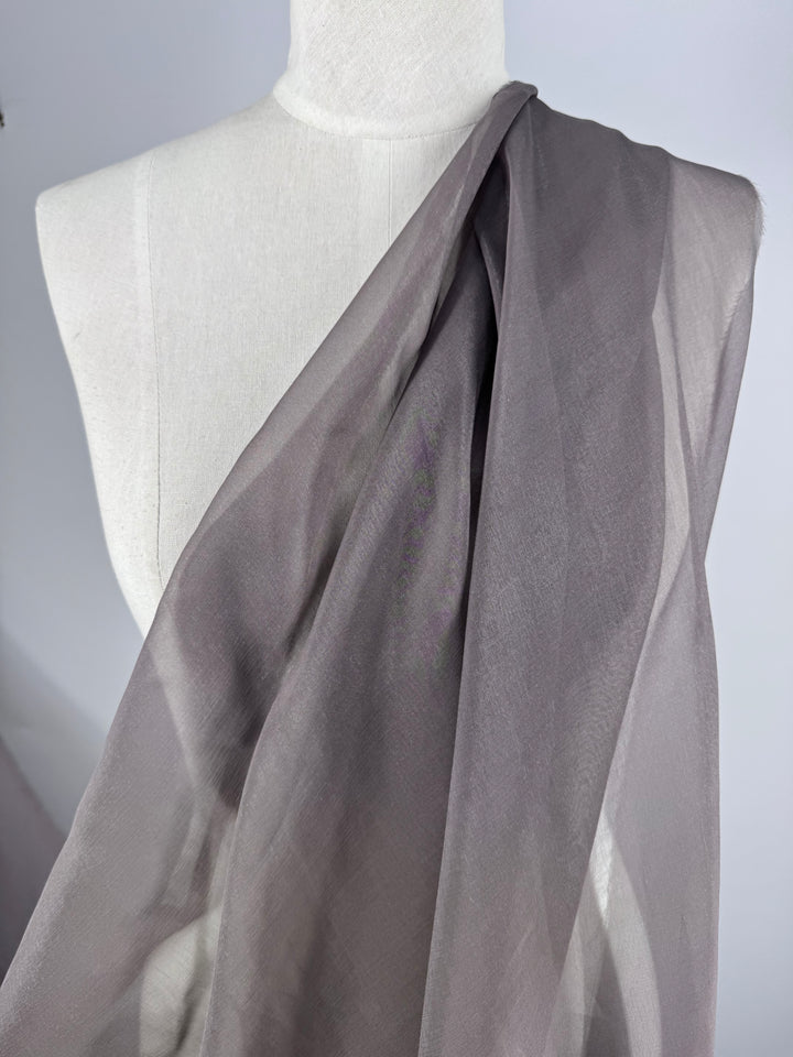 Blended Silk Mousseline - Pewter (147cm) from Super Cheap Fabrics, a sheer smoky gray fabric, drapes diagonally over a white dress form, creating soft elegant folds against a plain light background.