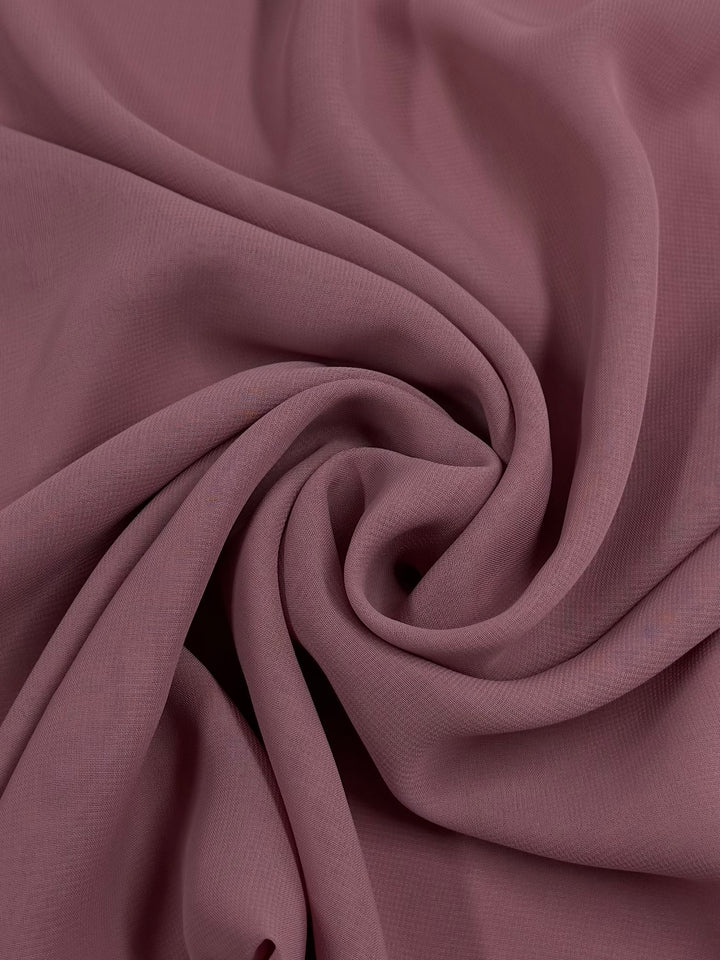 A close-up of Super Cheap Fabrics' Hi-Multi Chiffon in Blush (148cm), showing its soft, sheer mauve fabric with a smooth texture, elegantly gathered into gentle folds and swirling patterns at the center.
