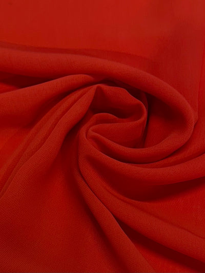 A close-up of Hi-Multi Chiffon - Tangerine Tango - 148cm by Super Cheap Fabrics shows bright red, lightweight fabric swirled and folded, revealing soft curves and shadows—a vibrant tribute to sheer fabric in Tangerine Tango.