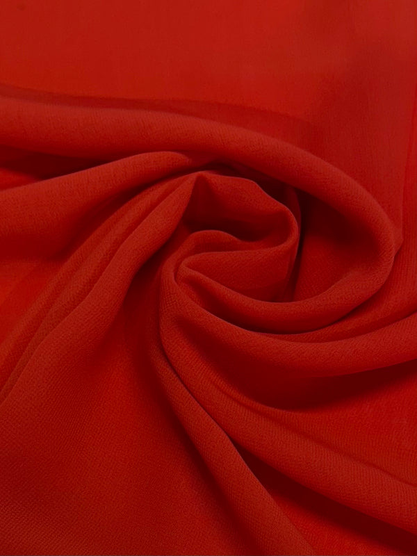 A close-up of Hi-Multi Chiffon - Tangerine Tango - 148cm by Super Cheap Fabrics shows bright red, lightweight fabric swirled and folded, revealing soft curves and shadows—a vibrant tribute to sheer fabric in Tangerine Tango.