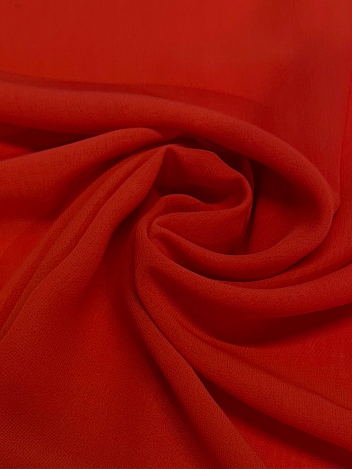 A close-up of Hi-Multi Chiffon - Tangerine Tango - 148cm by Super Cheap Fabrics shows bright red, lightweight fabric swirled and folded, revealing soft curves and shadows—a vibrant tribute to sheer fabric in Tangerine Tango.