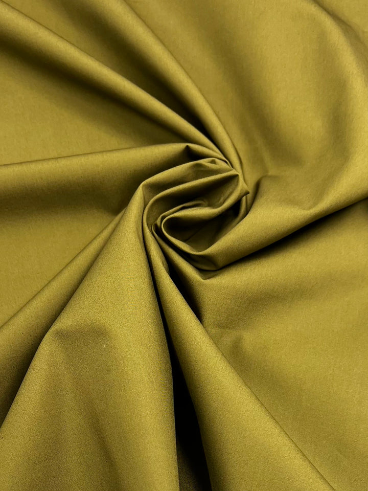 Close-up of Plain Cotton - Olive - 147cm by Super Cheap Fabrics, featuring a smooth, lightweight texture. The olive fabric is softly gathered in the center, creating gentle folds and a swirling pattern—an elegant display of quality cotton.