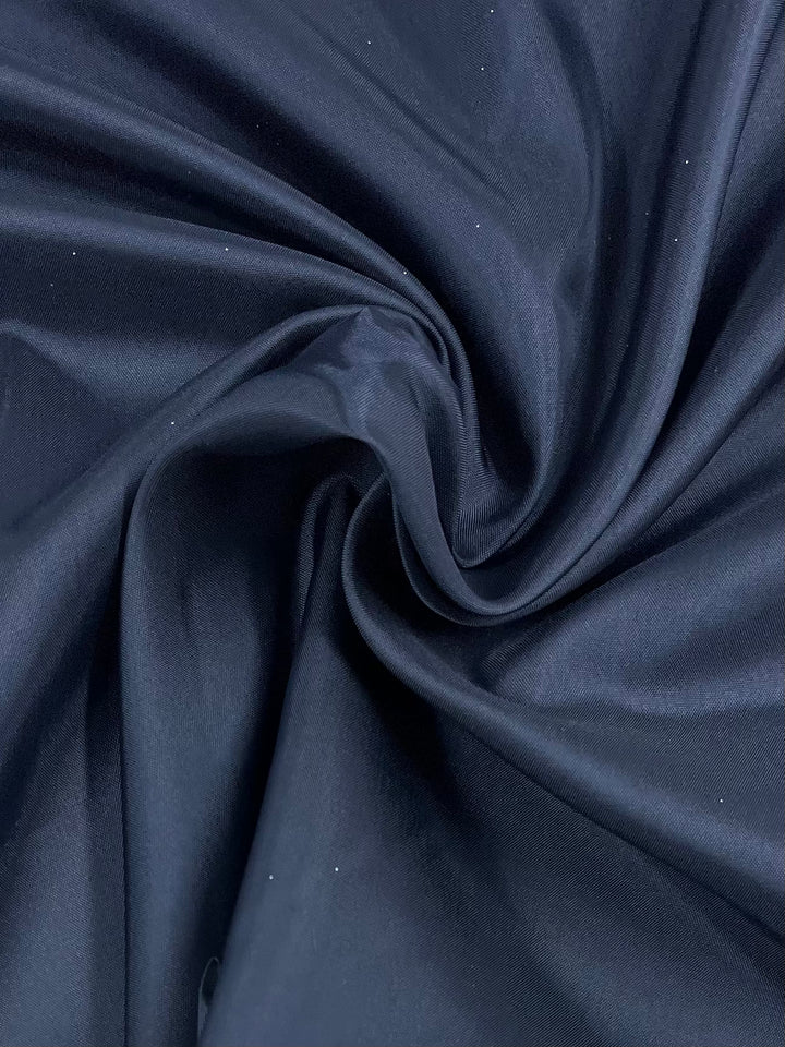 Close-up view of a piece of "Lining - Navy - 120cm" from Super Cheap Fabrics draped and gathered to form soft folds and ripples, showcasing its smooth and shiny texture.