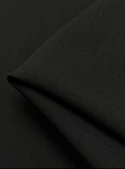 Close-up of the Stretch Crepe - Raven by Super Cheap Fabrics, showcasing its smooth, folded black fabric with an elegant matte finish, forming a sharp corner against a dark background.
