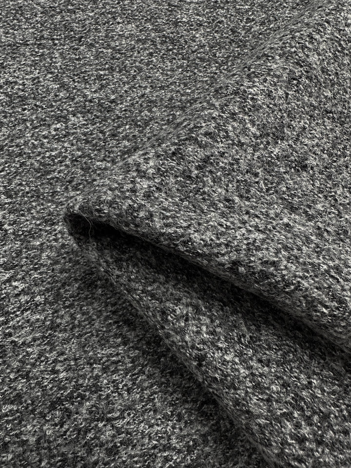 Close-up image of folded, speckled grey Boiled Wool - Charcoal Marle - 140cm by Super Cheap Fabrics with a soft, textured surface. The fabric has a slightly heathered appearance, blending light and dark grey fibers for a subtle, mottled effect. Perfect for autumn/winter clothing, the heavy-weight wool's edges are clearly visible.