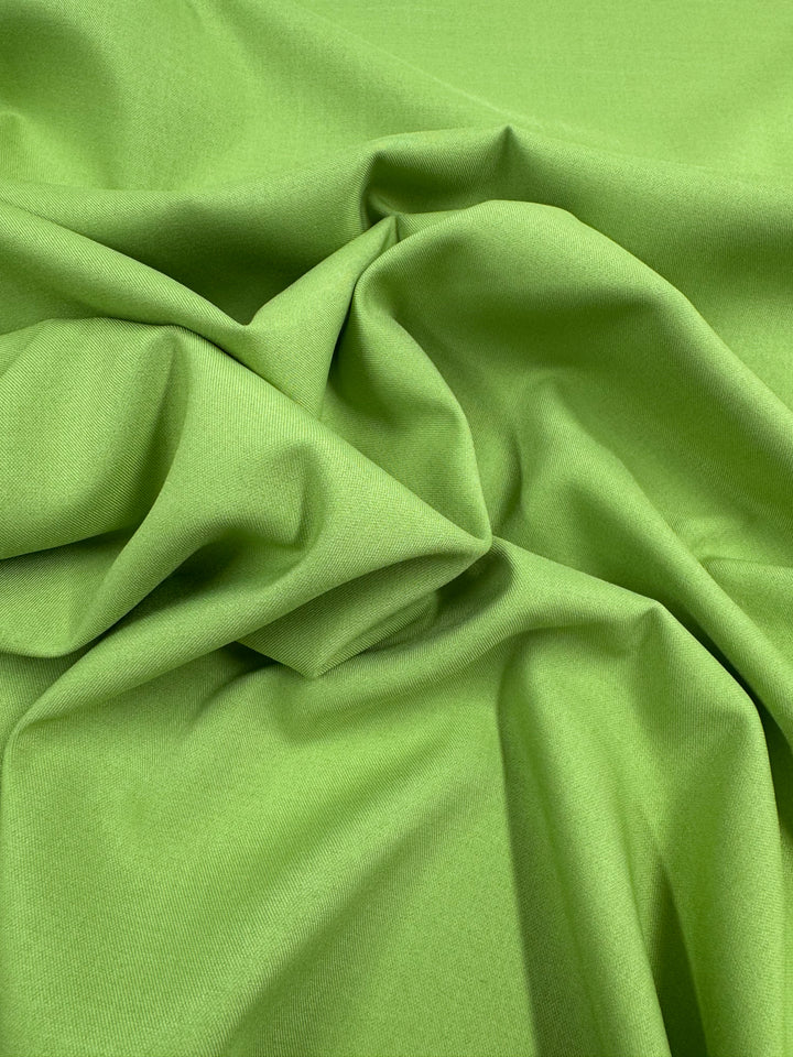 Super Cheap Fabrics' Twill Suiting - Green Glow (150cm) features bright green polyester with a soft texture, loosely gathered to create gentle folds and highlight its diagonal twill weave.