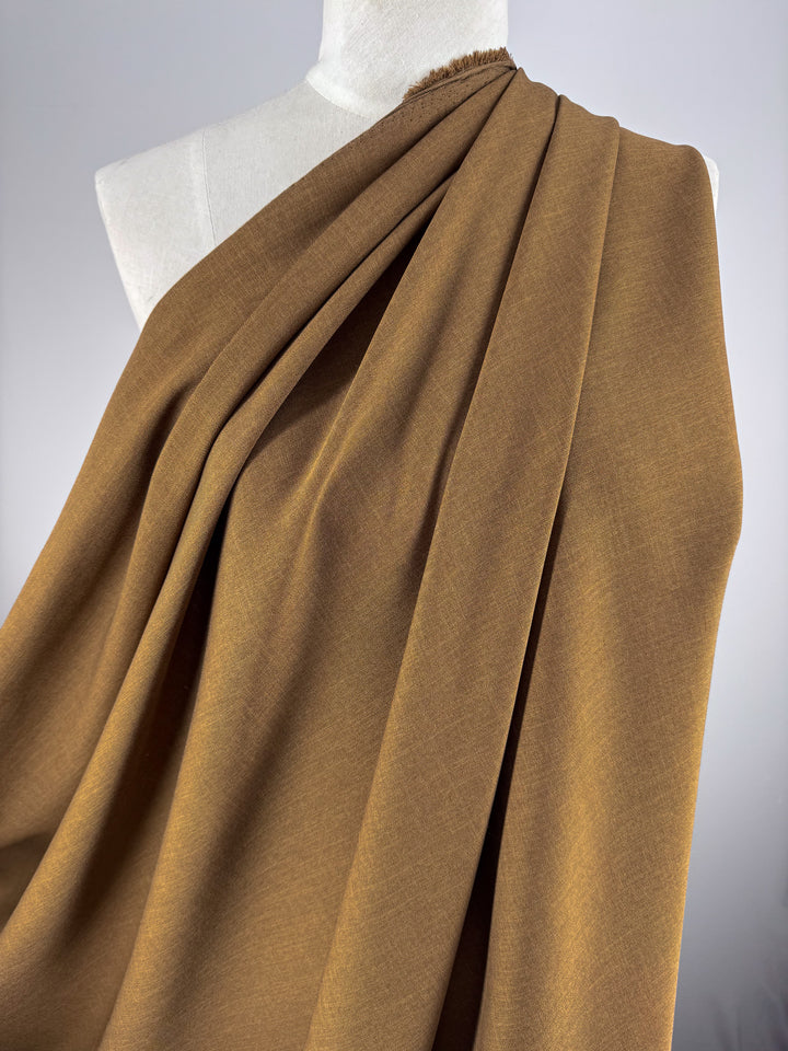 Super Cheap Fabrics’ Twill Suiting - Raw Hide (150cm), a brown polyester fabric with a subtle diagonal weave, is draped over a white dress form, highlighting its smooth texture and soft folds against a plain, light backdrop.