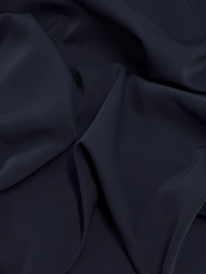 A close-up of Super Cheap Fabrics' Microfibre Suiting - Navy - 150cm shows dark navy polyester with soft folds and a smooth texture, creating gentle shadows and highlights.