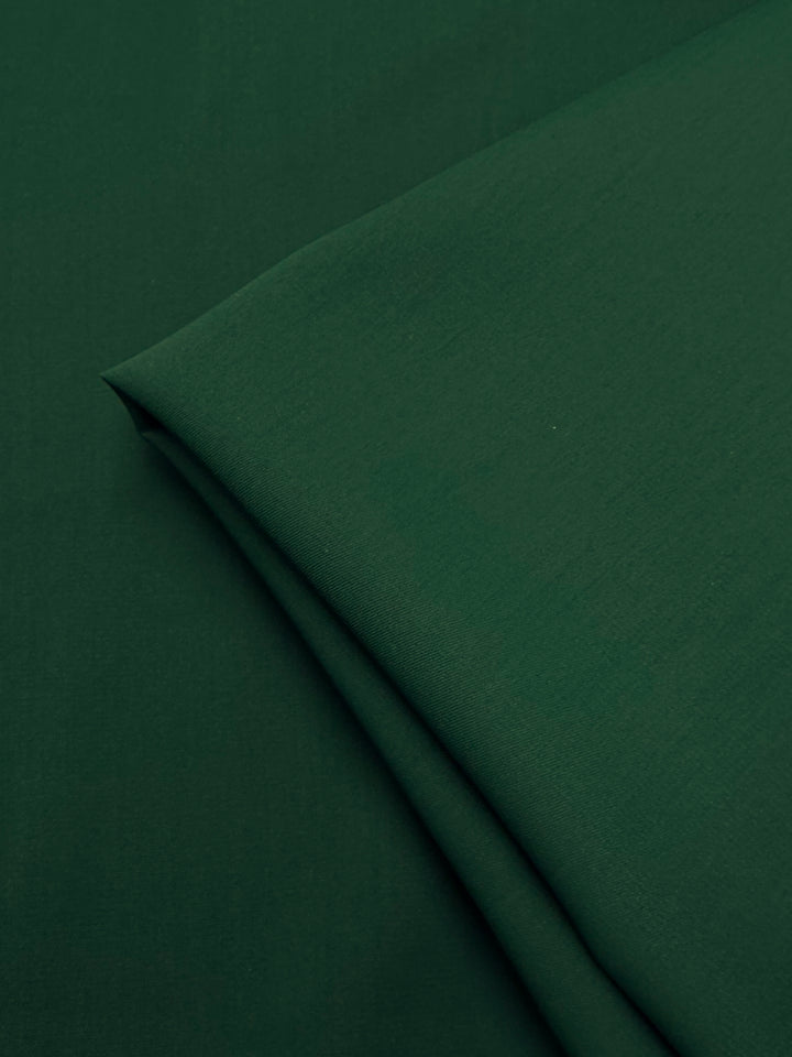 A close-up of Super Cheap Fabrics’ Microfibre Suiting in Dark Green (150cm), showing the lightweight polyester’s smooth surface and subtle texture as it rests folded on a matching background.
