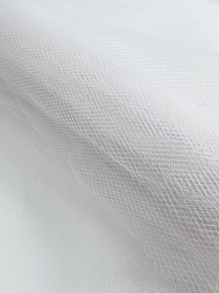 A close-up of Super Cheap Fabrics' Soft Tulle - White - 150cm, featuring a fine net pattern softly layered over white—perfect for costumes or delicate bridal veils.