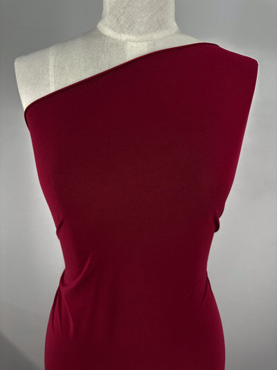 A torso mannequin showcases a fitted, one-shoulder dress made from Super Cheap Fabrics’ ITY Knit - Red Bud (150cm), featuring medium weight and a smooth feel, set against a plain gray background.