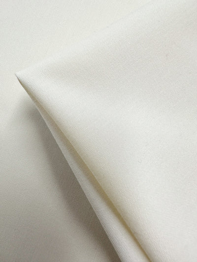 A close-up of Suiting - Pristine - 150cm from Super Cheap Fabrics, showing its smooth, slightly textured ivory surface and soft weave—ideal for medium weight garments.