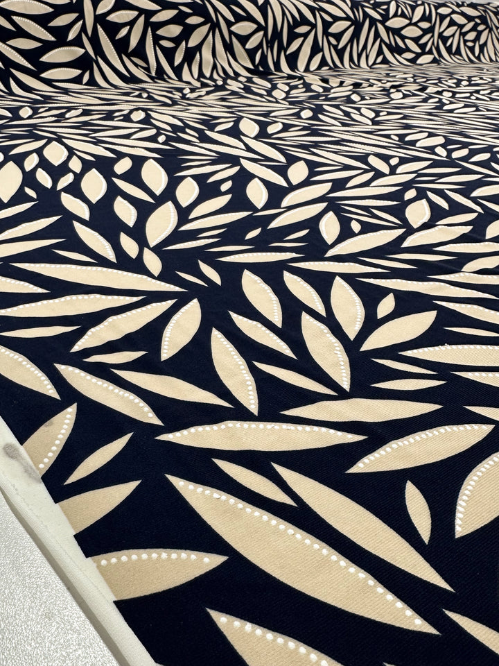 A close-up of Super Cheap Fabrics’ Textured Lycra - Prism Leaf (150cm), a medium-weight Polyester/Spandex with overlapping beige leaf motifs and dotted lines on dark navy, creating a bold, textured abstract look.