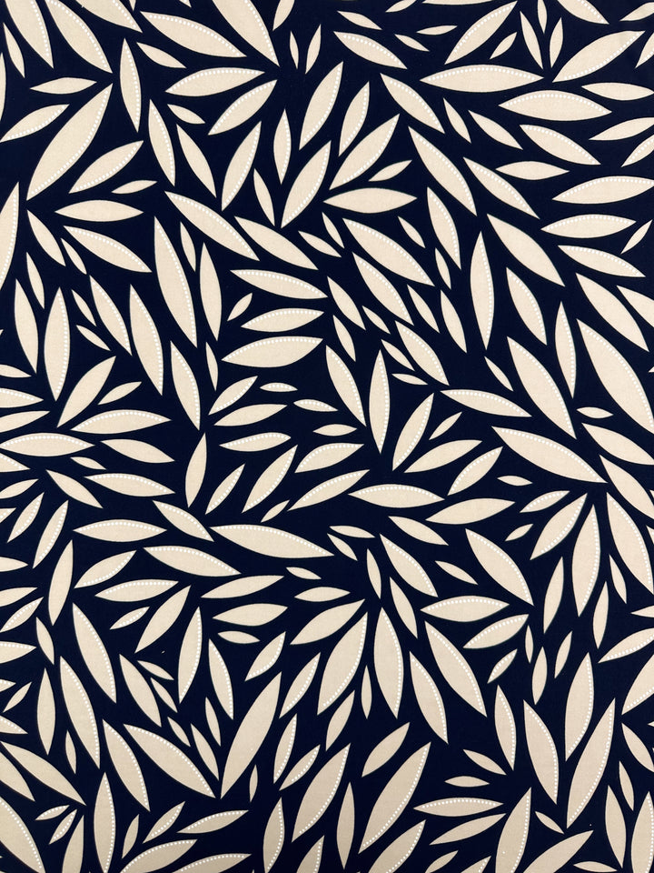 The Textured Lycra - Prism Leaf by Super Cheap Fabrics features cream elongated leaf motifs on a dark navy background in a dense, overlapping foliage design, made from medium-weight Polyester/Spandex, 150cm wide.