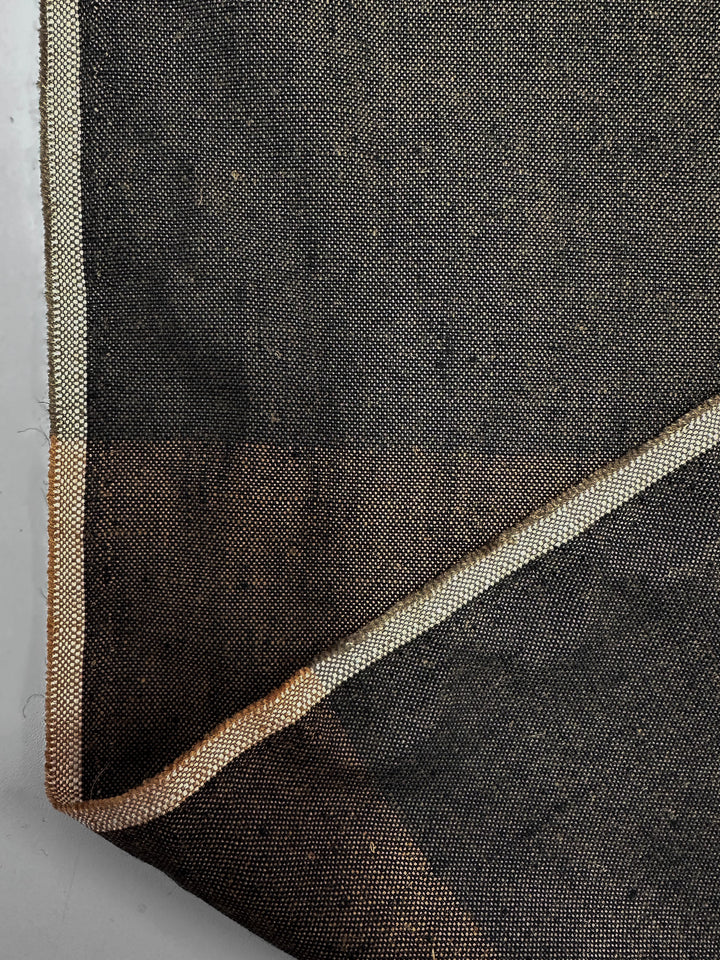 Close-up of Super Cheap Fabrics' Linen Viscose - Rustline Canvas (145cm), showing the heavy-weight, visible weave fabric with a folded corner revealing lighter edge trim. Perfect for upholstery or clothing, displayed on a plain light surface.