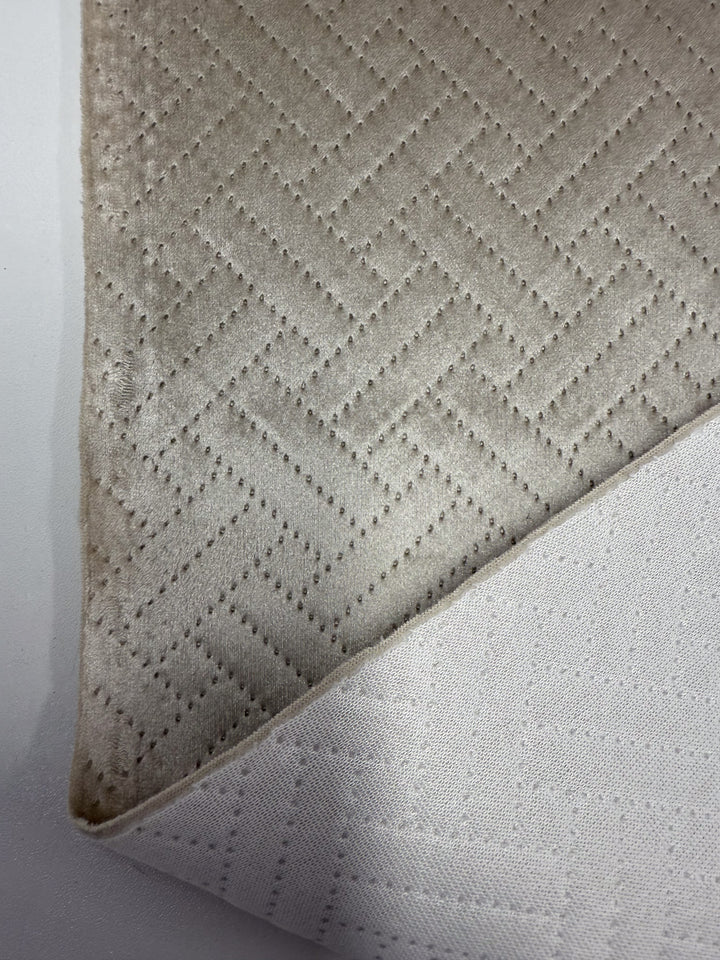 A close-up of two overlapping Super Cheap Fabrics’ Embossed Velvet - Oatmeal (150cm) pieces, both with a subtle geometric zigzag. The top is beige, the bottom off-white—perfect for upholstering sofas and armchairs.