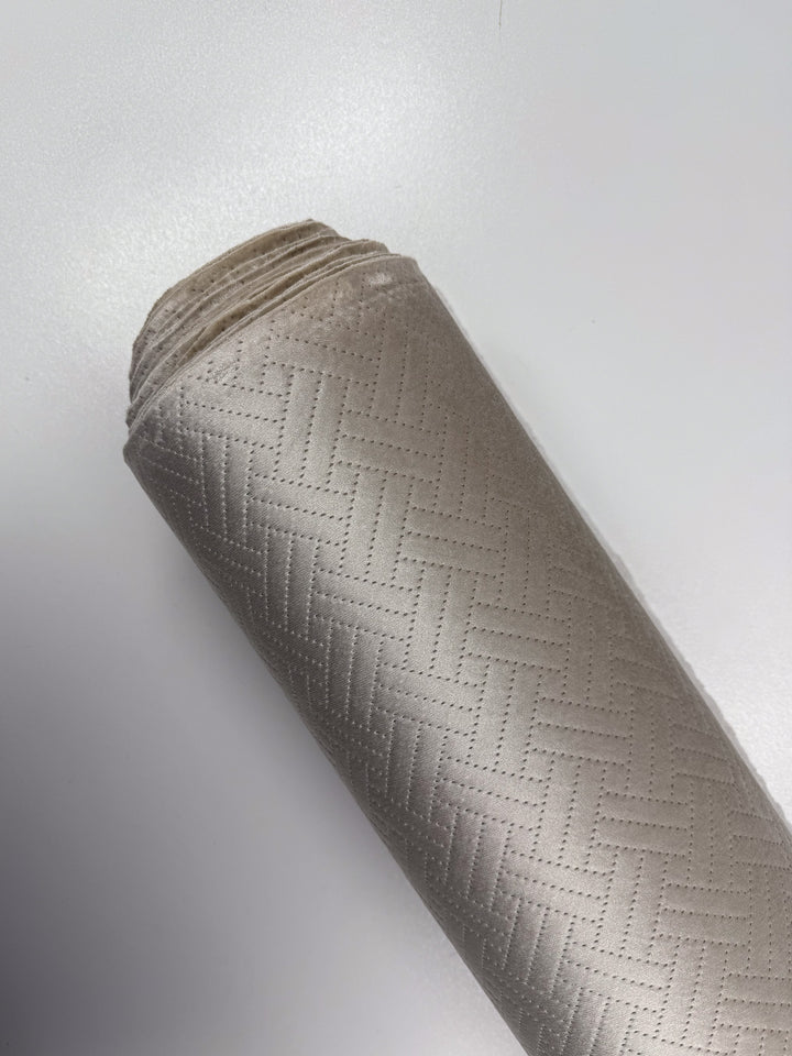 A close-up of Embossed Velvet - Oatmeal (150cm) by Super Cheap Fabrics, featuring a subtle geometric basket-weave pattern, reminiscent of designer deadstock fabrics, resting on a white surface.
