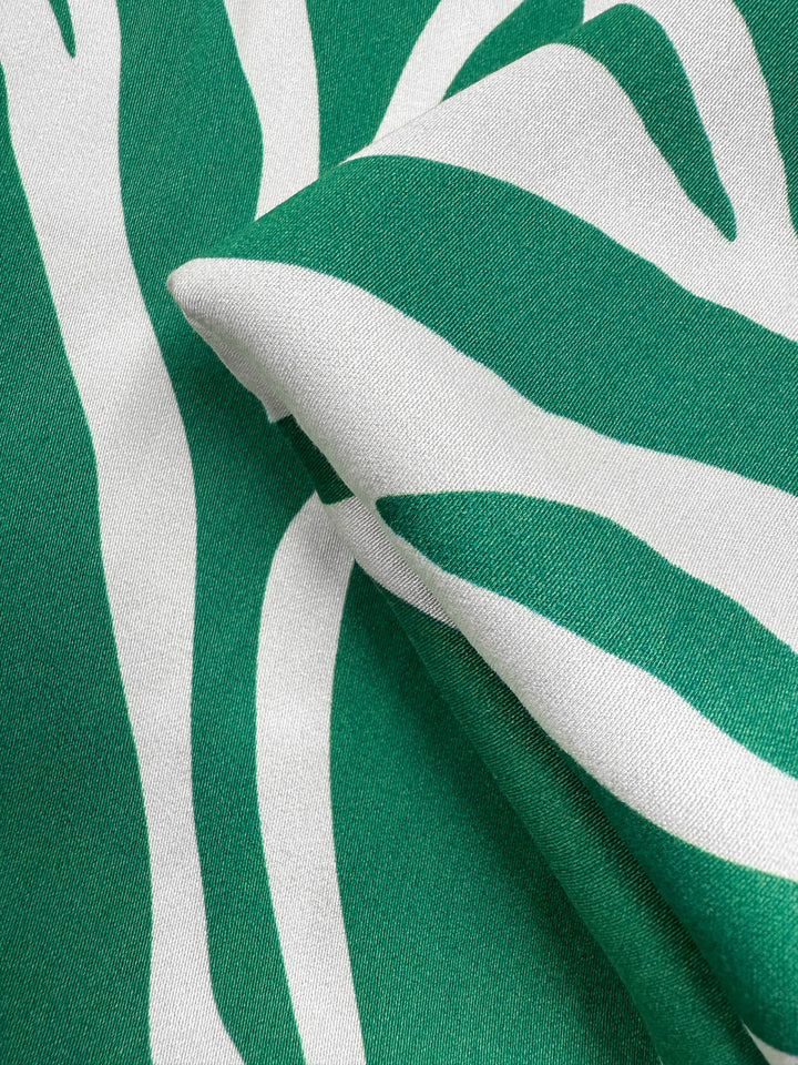 Close-up of Super Cheap Fabrics’ Mercerised Rayon - Tropic Cutout (150cm), featuring green and white breathable rayon with abstract, wavy zebra-like stripes and a folded texture that highlights its color contrast.