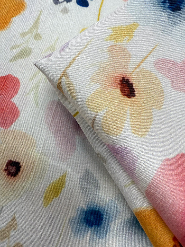 A close-up of Super Cheap Fabrics' Mercerised Rayon - Meadowdrop (150cm), showing lightweight, slightly shiny, smooth fabric with a pastel floral print in yellow, pink, red, and blue flowers on a light background.