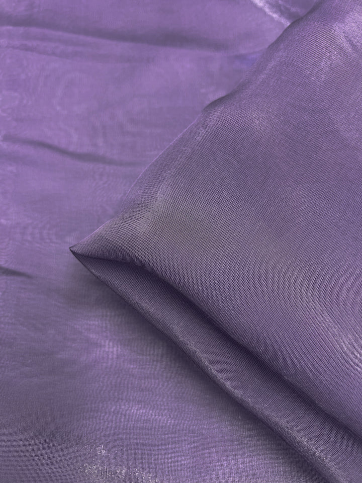 A folded piece of Silk Mousseline - Currant from Super Cheap Fabrics is elegantly draped on a matching purple surface, creating a seamless and luxurious appearance. Its extra lightweight nature enhances the elegance, making it perfect for crafting bespoke dresses.