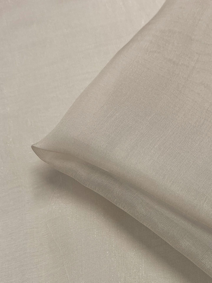 A close-up of Super Cheap Fabrics’ Silk Mousseline in Mushroom (140cm) showcases its extra lightweight, sheer, and soft texture. The fabric is folded neatly on a matching background, emphasizing its delicate quality.