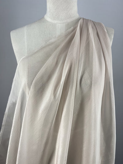 Super Cheap Fabrics' Silk Mousseline - Mushroom - 140cm is a sheer, extra-lightweight silk that drapes diagonally on a dress form, creating soft folds and a delicate, translucent effect against a plain background.