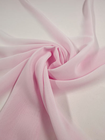 The Hi-Multi Chiffon - Cradle Pink - 150cm from Super Cheap Fabrics is a light pink sheer polyester, artfully spiraled on a white surface to showcase its soft folds and delicate texture.