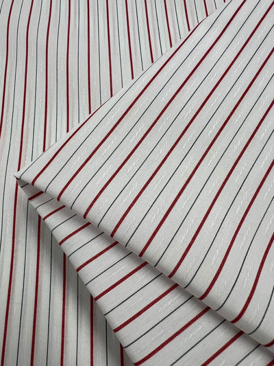 Super Cheap Fabrics’ Shirting - Pins - 145cm is a lightweight white polyester cotton with red and black vertical stripes, subtle woven texture, and neatly folded corners—perfect for versatile projects.