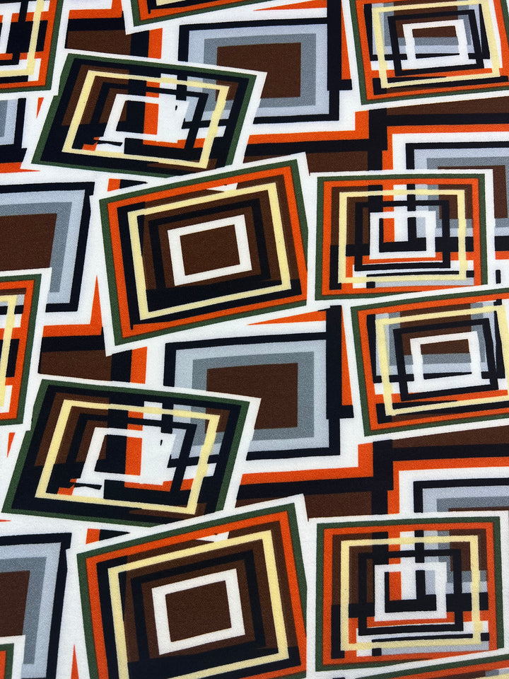 The Printed Crepe - Geo Repeat by Super Cheap Fabrics features an abstract pattern with overlapping rectangles in orange, brown, gray, black, and white. Crafted from lightweight fabric echoing high fashion trends, the design showcases varied sizes and orientations for a dynamic effect.