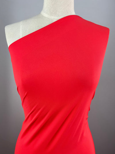 A close-up of the Super Cheap Fabrics' Nylon Lycra dress in Fiery Red, displayed on a mannequin. The four-way stretch fabric appears smooth and form-fitting, with the left shoulder and collarbone exposed. The neutral background emphasizes the vibrant color and sleek design of this 155cm wide dress.